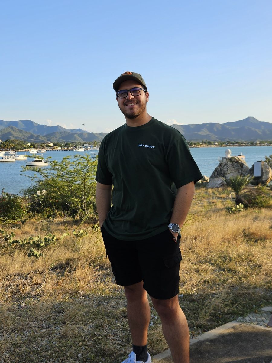 Pablo smiling by the bay in Juangriego, with boats and mountains behind him